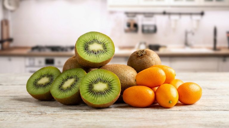 Assortiment de kiwis coupés en deux et de kumquats frais posés sur une table en bois dans une cuisine.