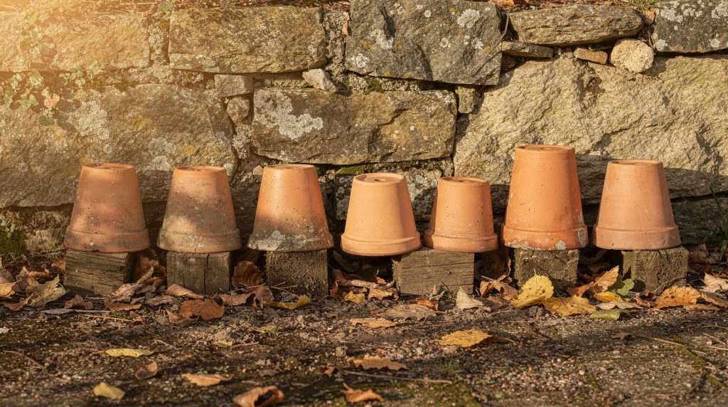 Rangée de pots en terre cuite retournés contre un mur de jardin en automne